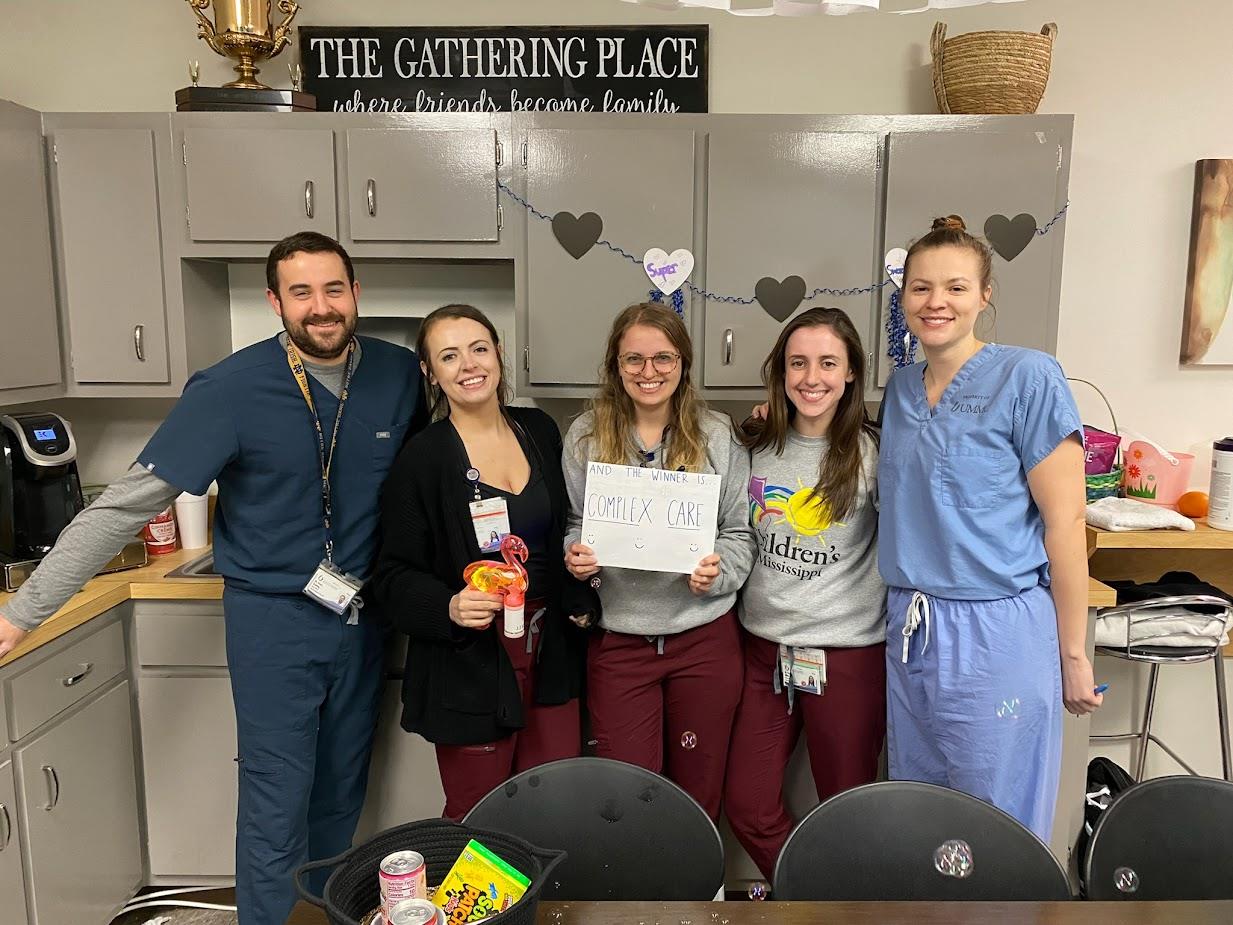 five pediatric residents in break room posing with sigh that reads And the Winner Is Complex Care